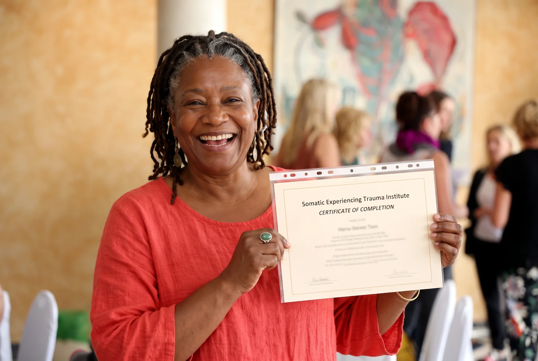 A joyful Somatic Experiencing participant holding her certificate of completion at a training gathering