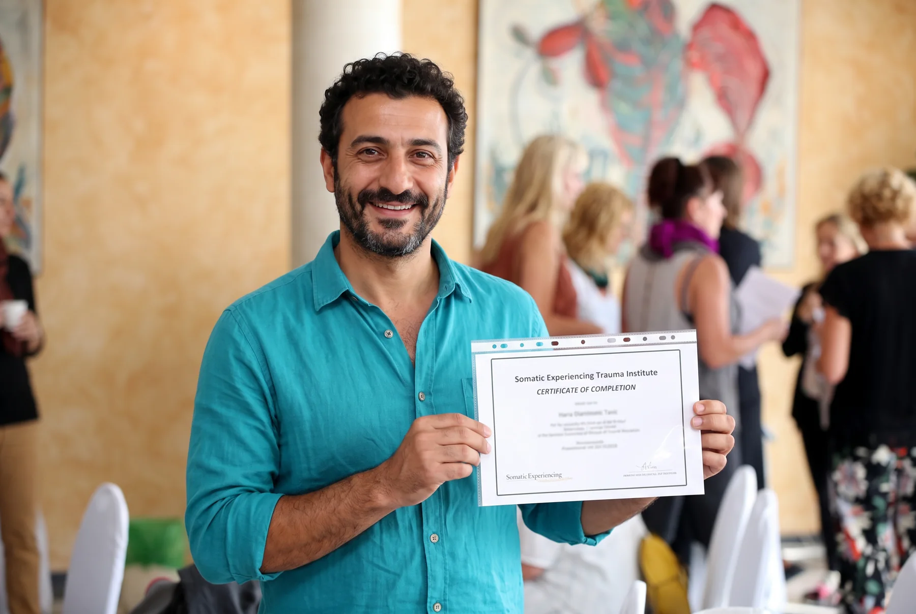 A smiling Somatic Experiencing participant holding his certificate of completion at a training gathering